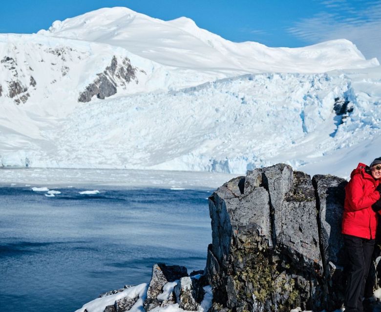 A couple of guests happily poses near grey rocks in Antarctica.