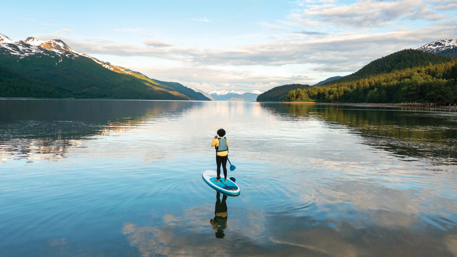 Woman paddleboarding on a glassy water lake on Alaska